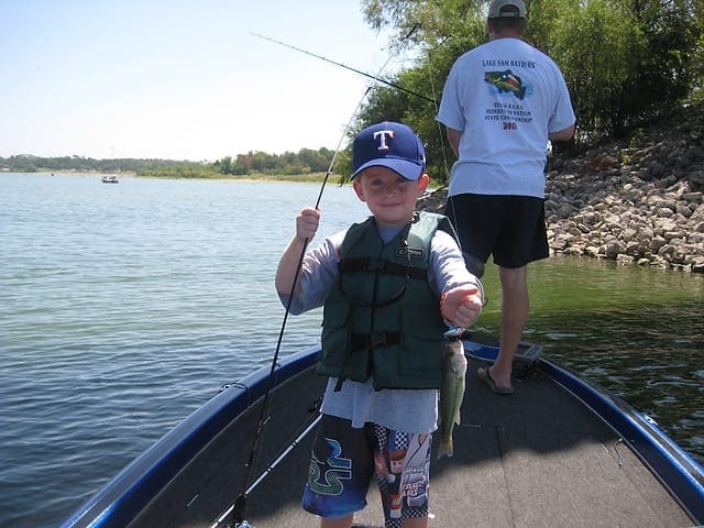 IT'S EASY: Taylor Hughs poses with a bass he caught while his dad, Mike Hughs, continues to try and catch a fish in the background. Photo by Bill Hughs. ssddds